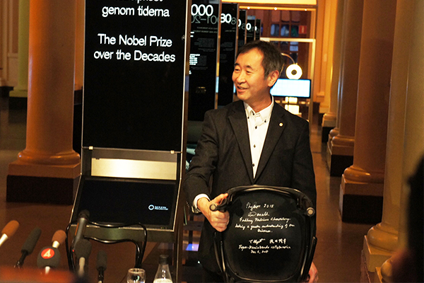 2015.12.06 Professor Kajita showing the chair with his signature and that of co-winner Professor Emeritus Arthur B. McDonald