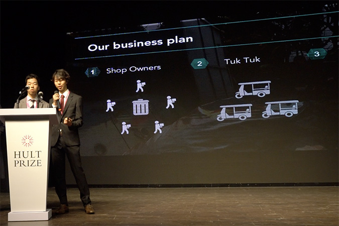 Two undergraduate students stand behind a podium on a dark stage.